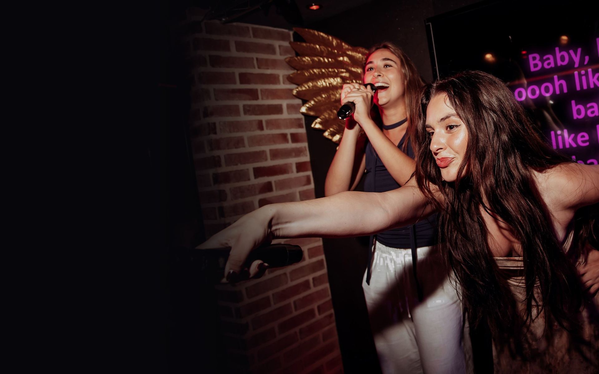 A guest sings on stage at Crystal’s while a friend dances in front of the lyrics screen