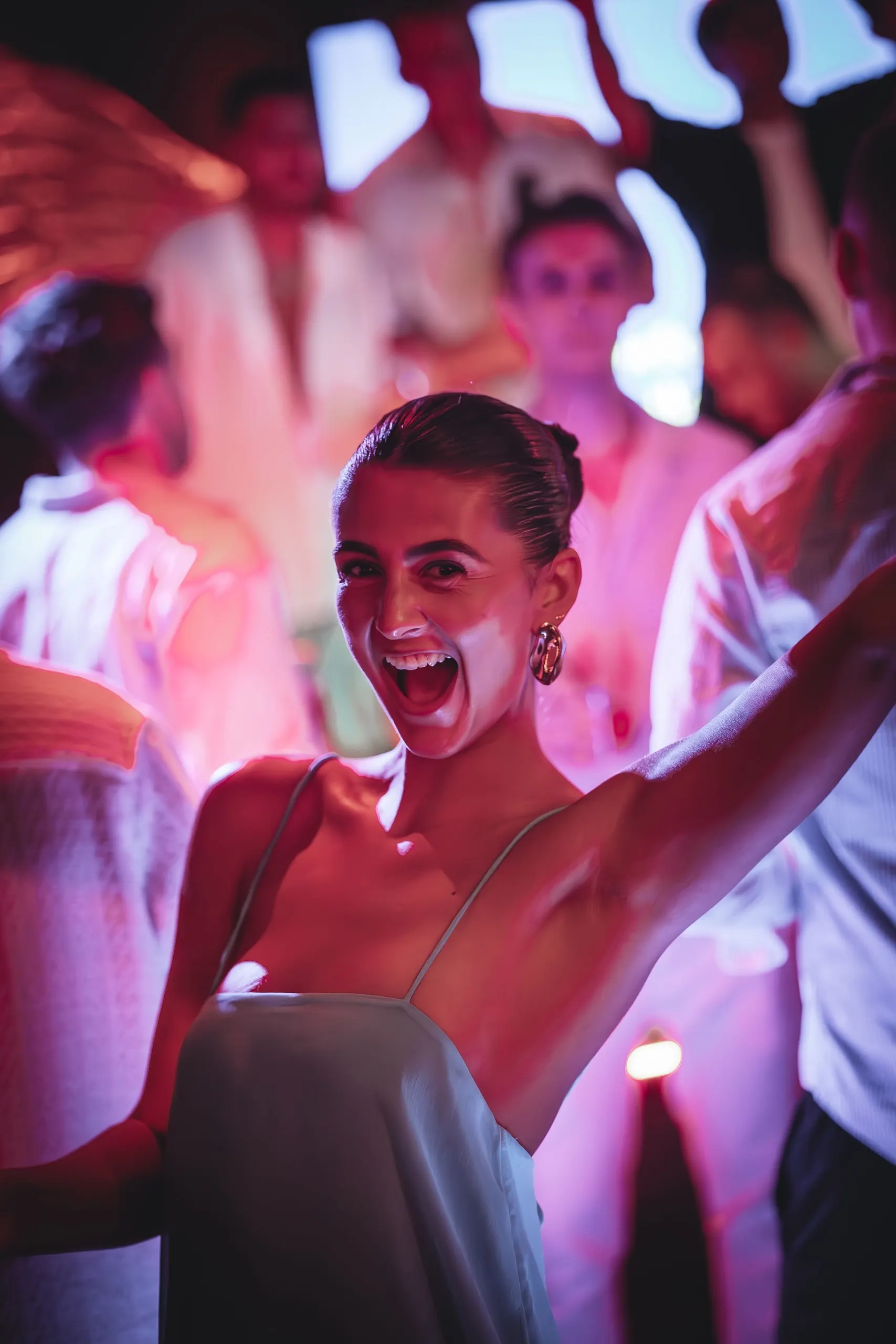 A guest cheers with one arm in the air under pink stage light